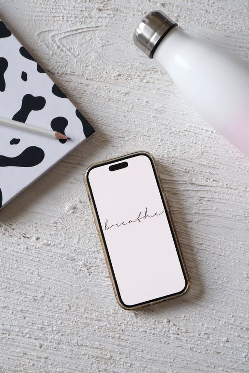 Free A serene minimalist setup featuring a smartphone displaying the word 'breathe', alongside a notebook and bottle. Stock Photo