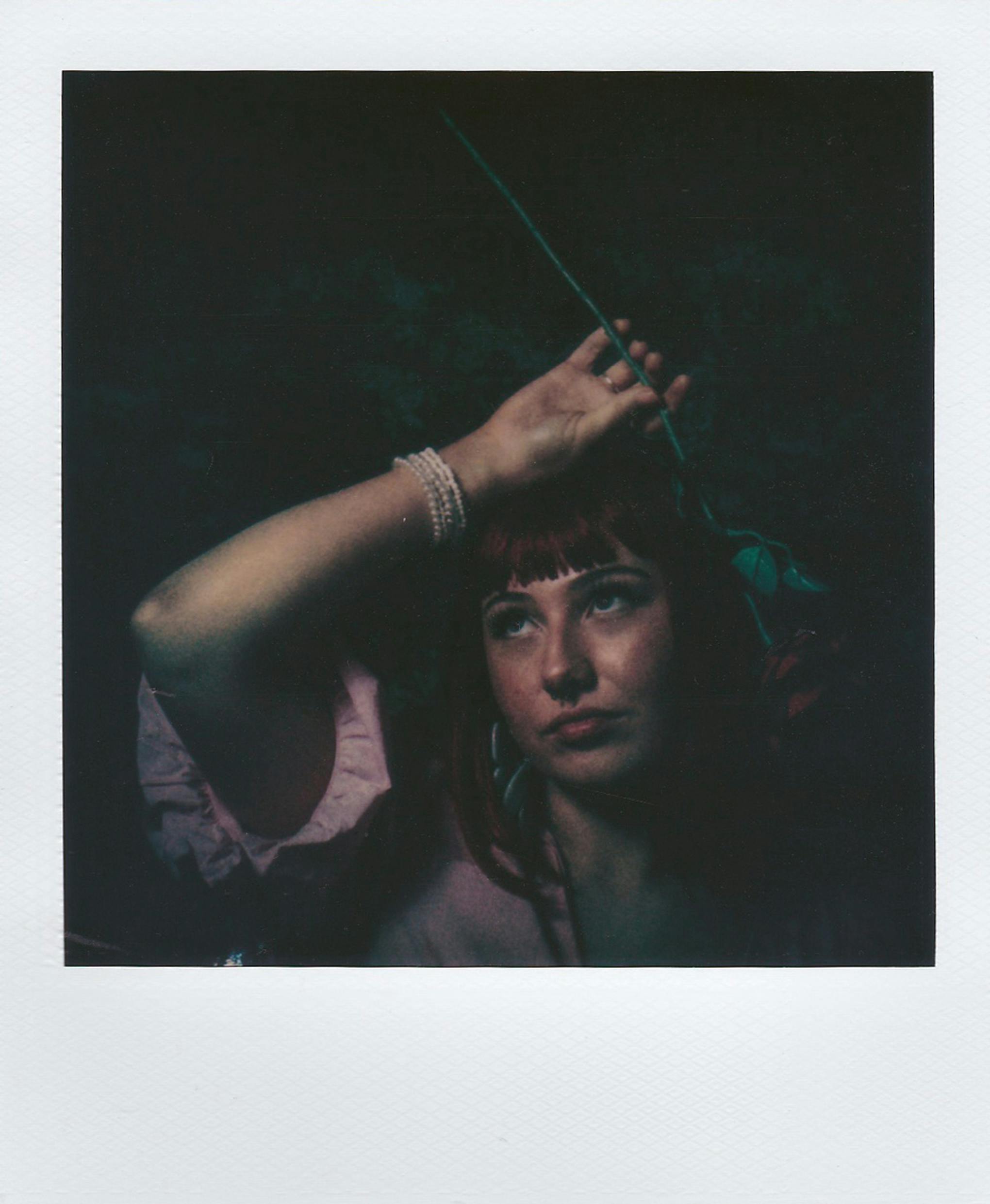 Moody portrait of a woman in pink dress holding a rose, evoking vintage style.