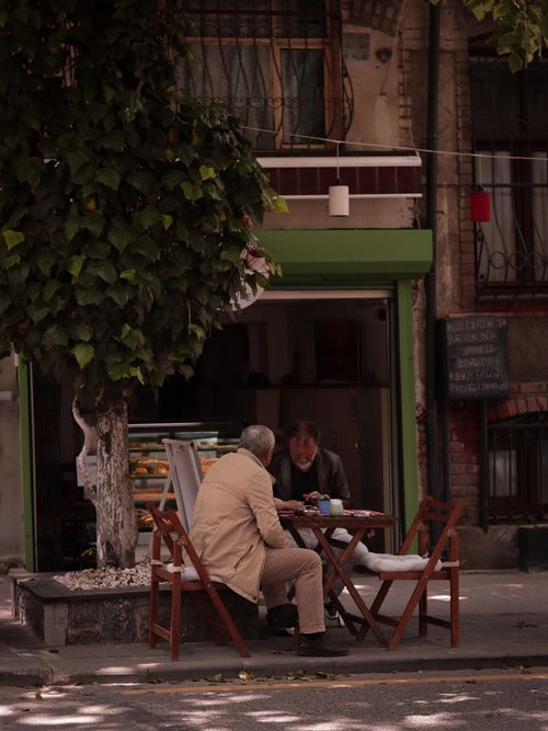 Free Two senior men converse at an outdoor cafe in a leafy urban area, enjoying leisure time. Stock Photo