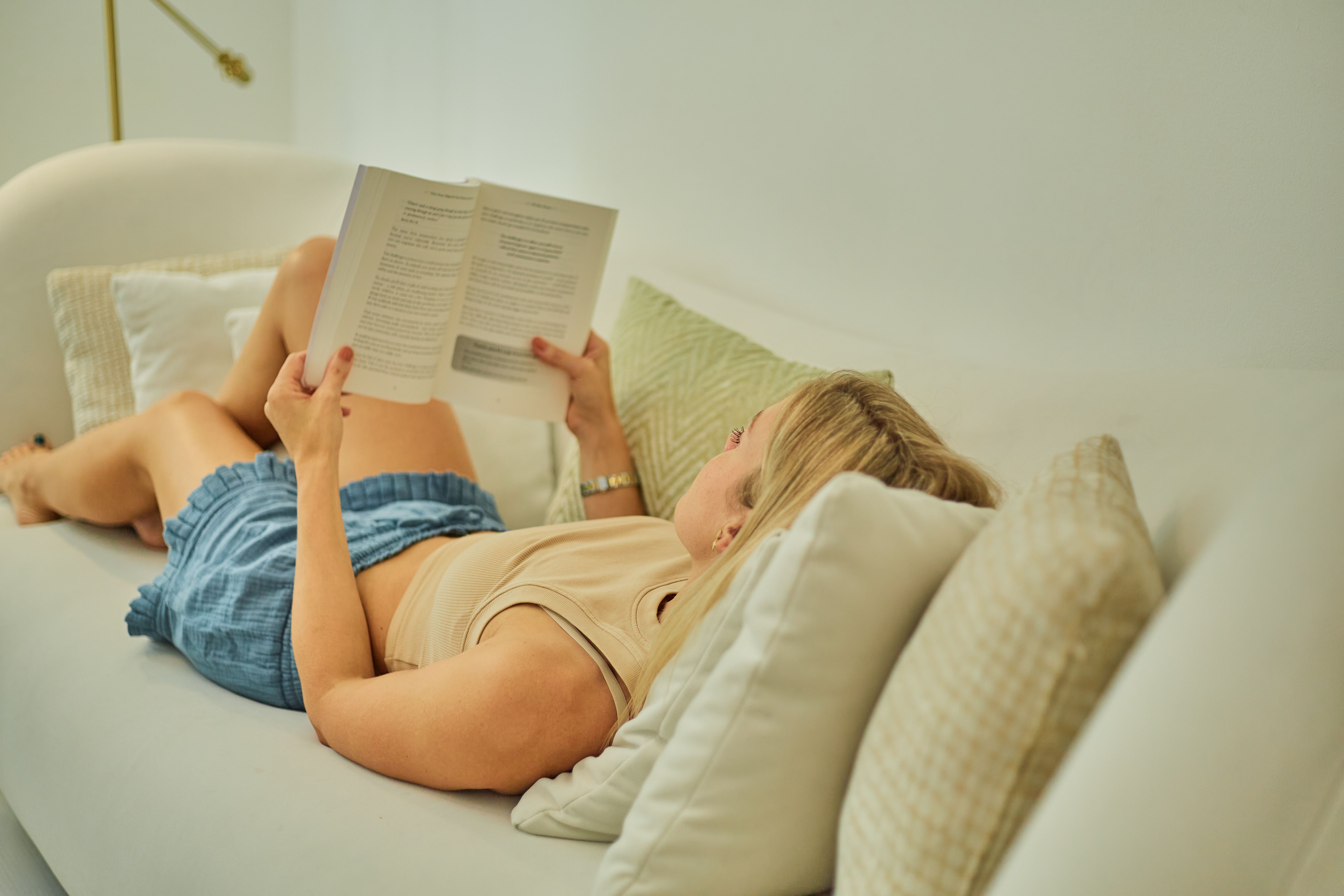 A woman reclines on a white sofa, enjoying a book in a peaceful, indoor setting.