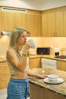Blonde woman in crop top enjoys coffee in a stylish kitchen setting.