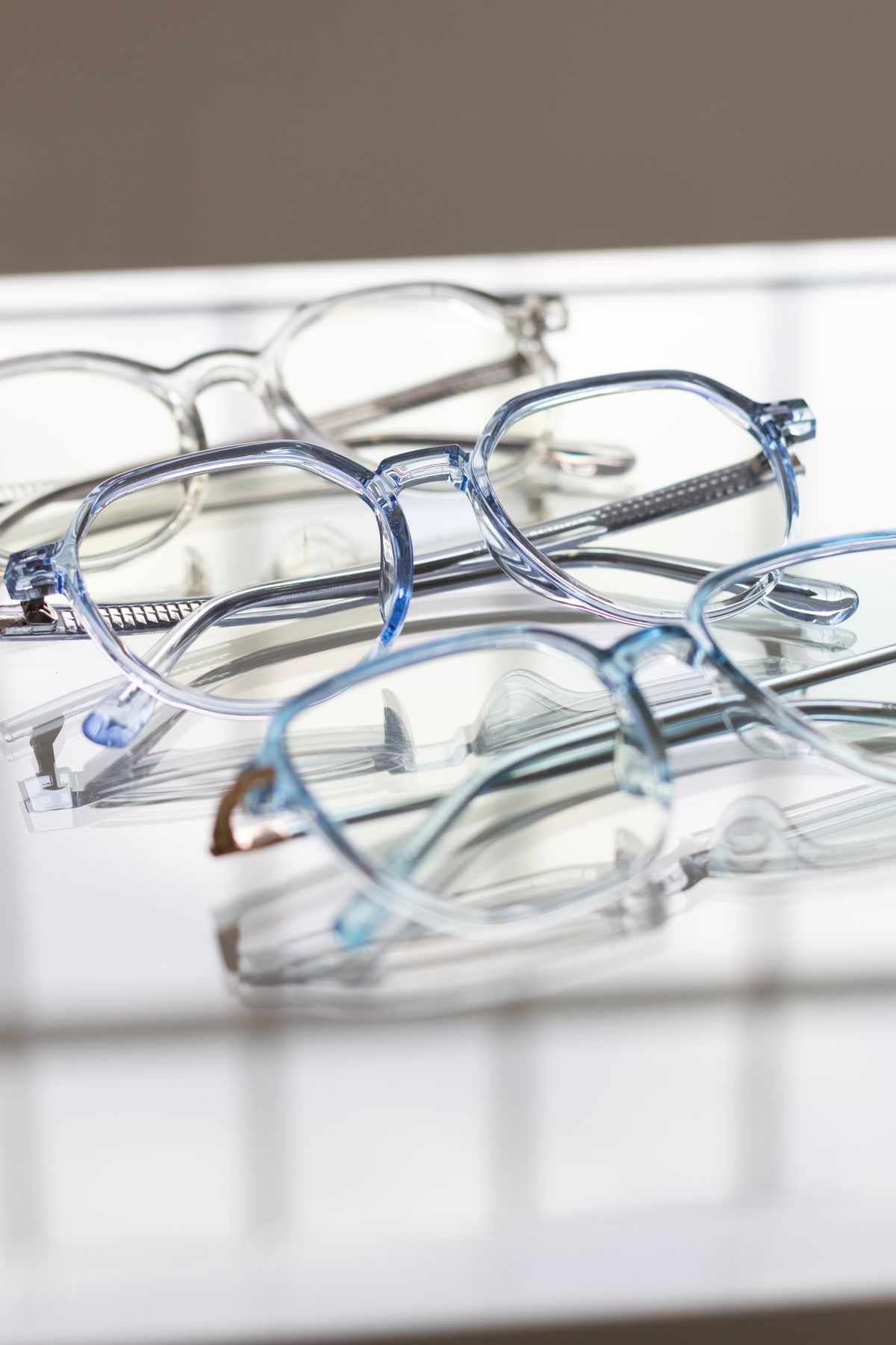 Varias monturas de gafas translúcidas y azuladas sobre una superficie reflectante