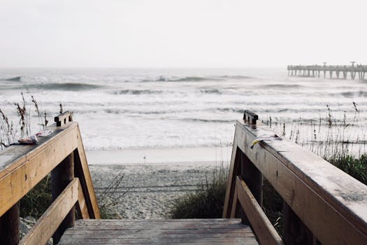 Scenic view of Jacksonville Beach pier with a wooden walkway, ocean waves, and sandy shore.