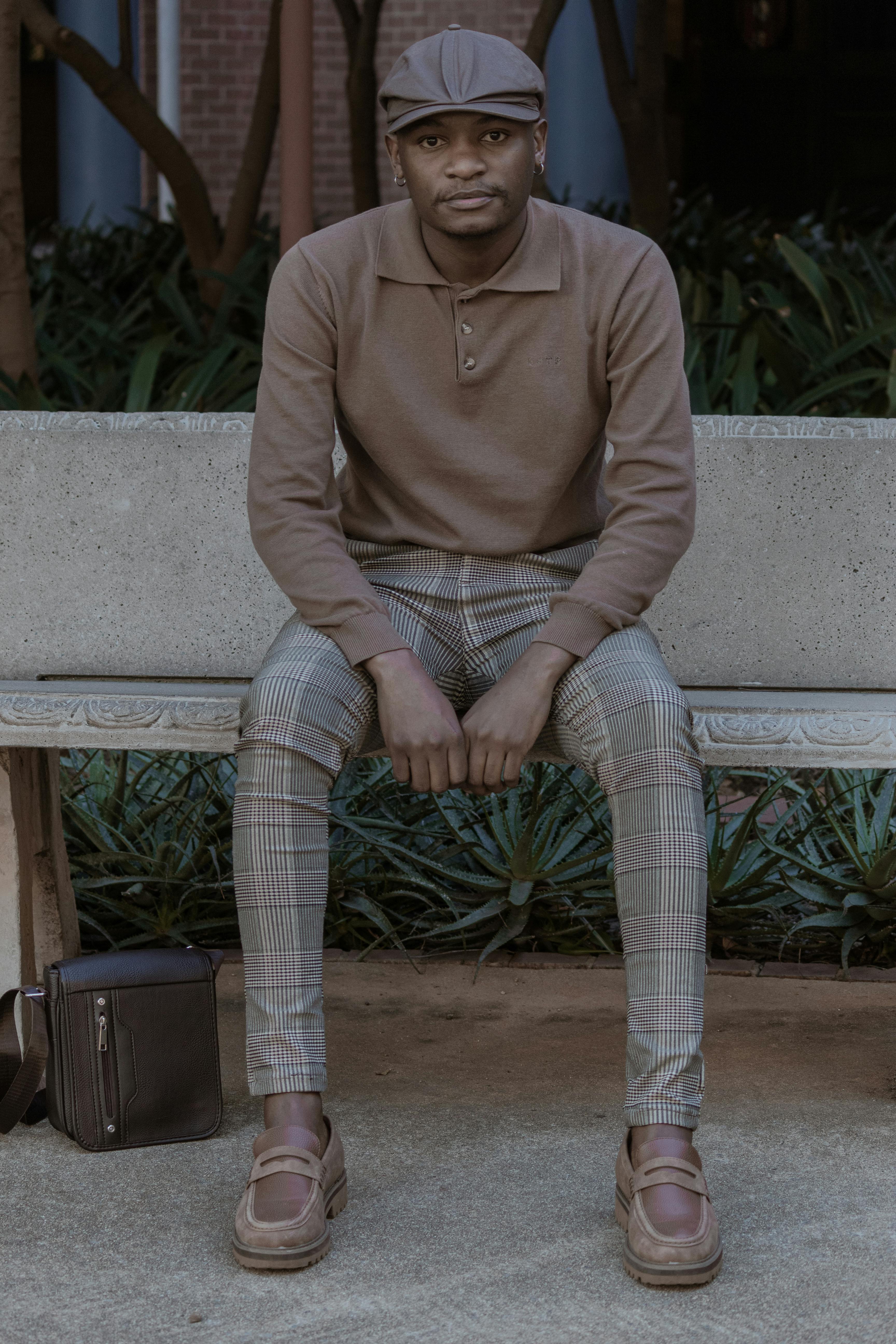 Fashionable man in casual wear sitting on a bench outdoors, showcasing urban style.