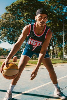 Athletic male playing basketball on an outdoor sunny court wearing sportswear.