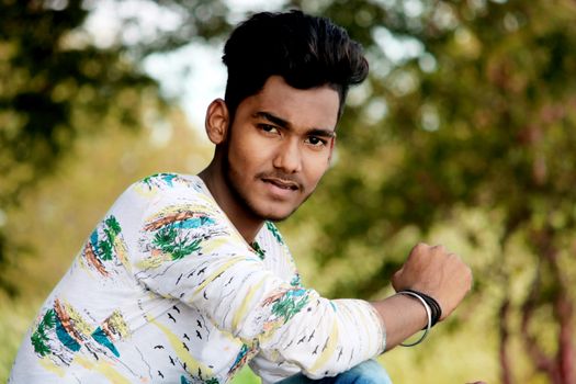 Portrait of a young man in a white patterned shirt enjoying a sunny day outdoors.