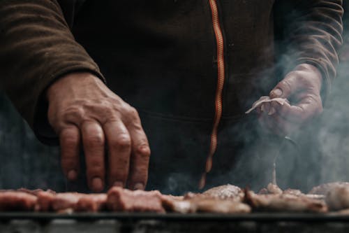 Man Hands over Meat on Barbecue
