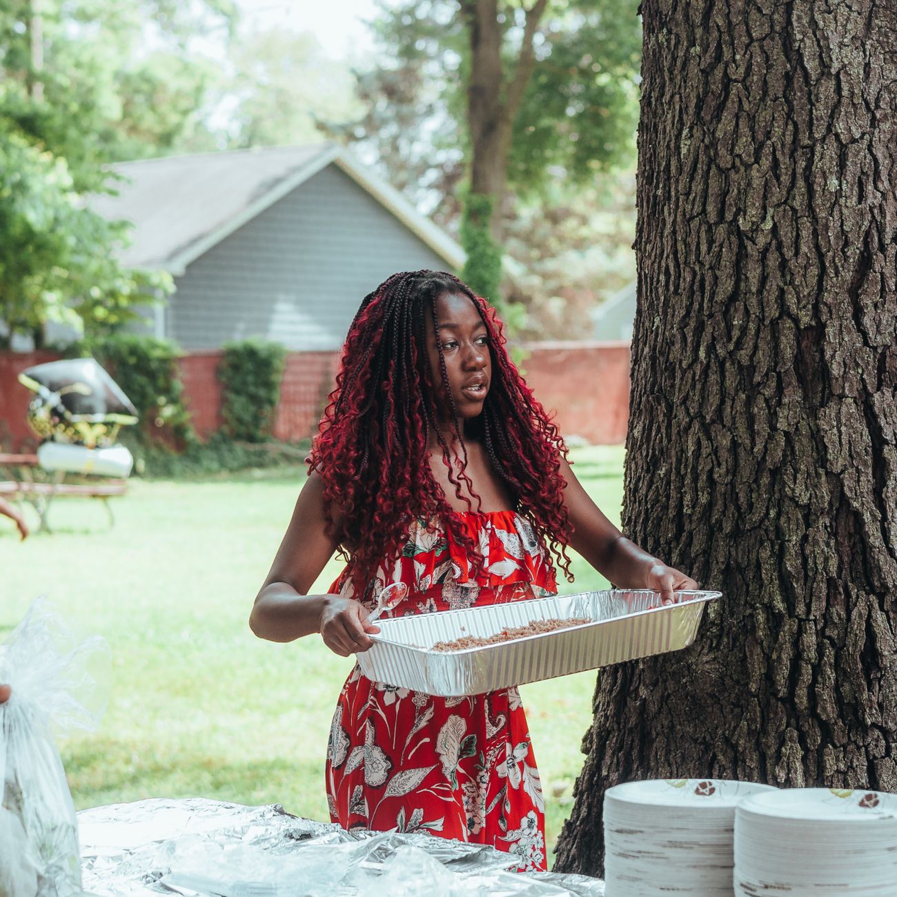 Woman holding food tray at a garden barbecue gathering on a sunny day.