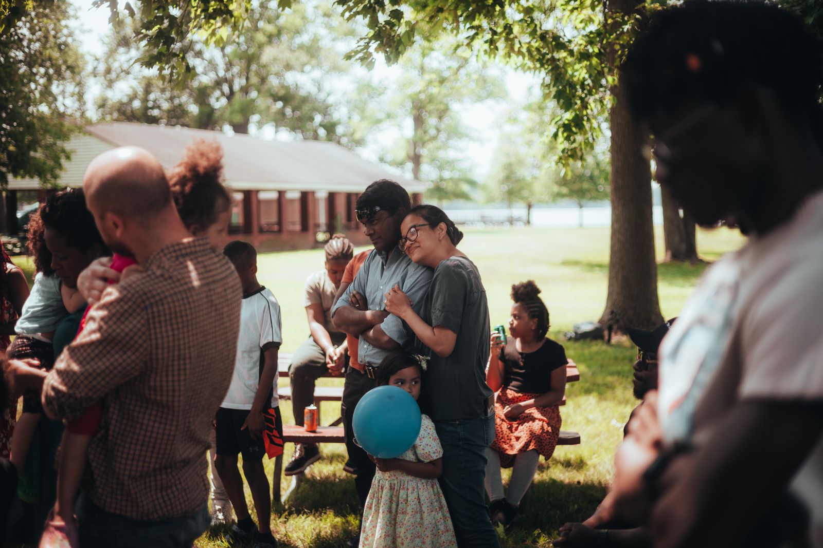 A multigenerational family gathered outdoors under shade trees at a summer family reunion in a park