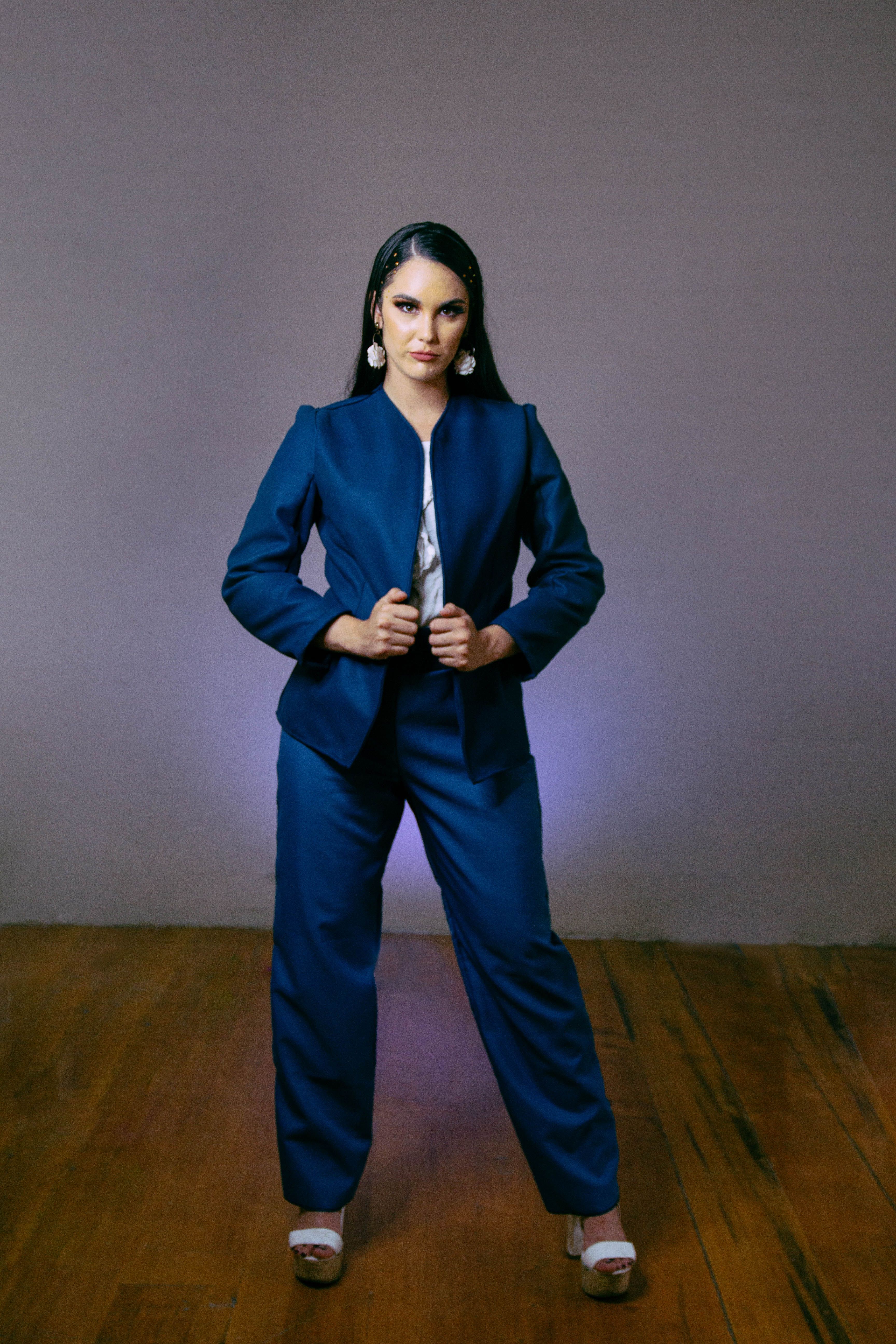 Confident woman in blue suit posing against a gray wall. Fashion photography.