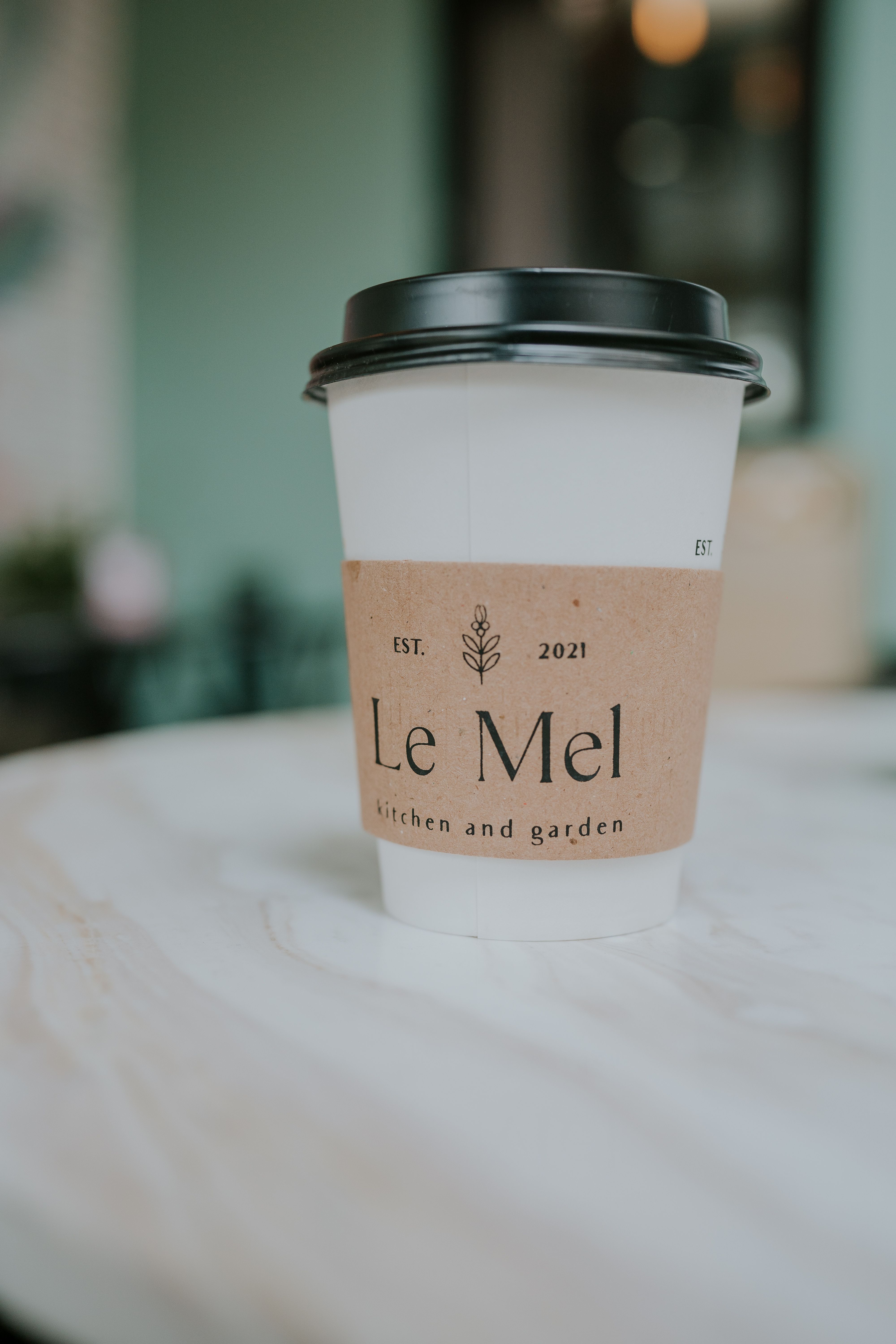 A paper coffee cup with a lid on a marble table in a cozy café setting.