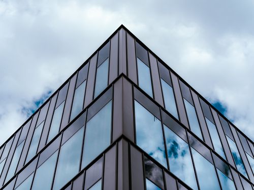 Free Low-angle view of a modern glass building with reflective windows under an overcast sky. Stock Photo