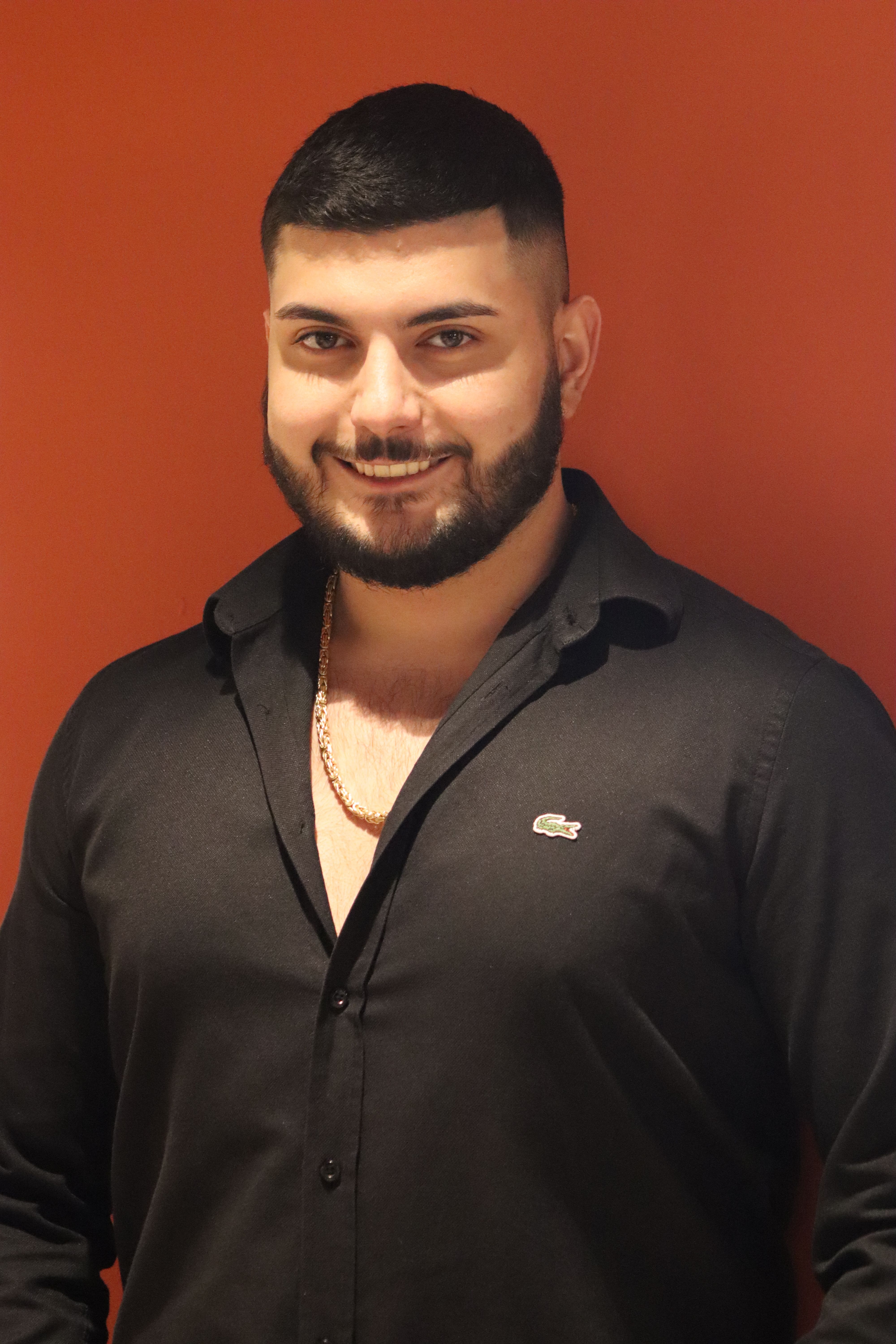 Portrait of a smiling man in a black shirt with an orange background during a studio shoot.