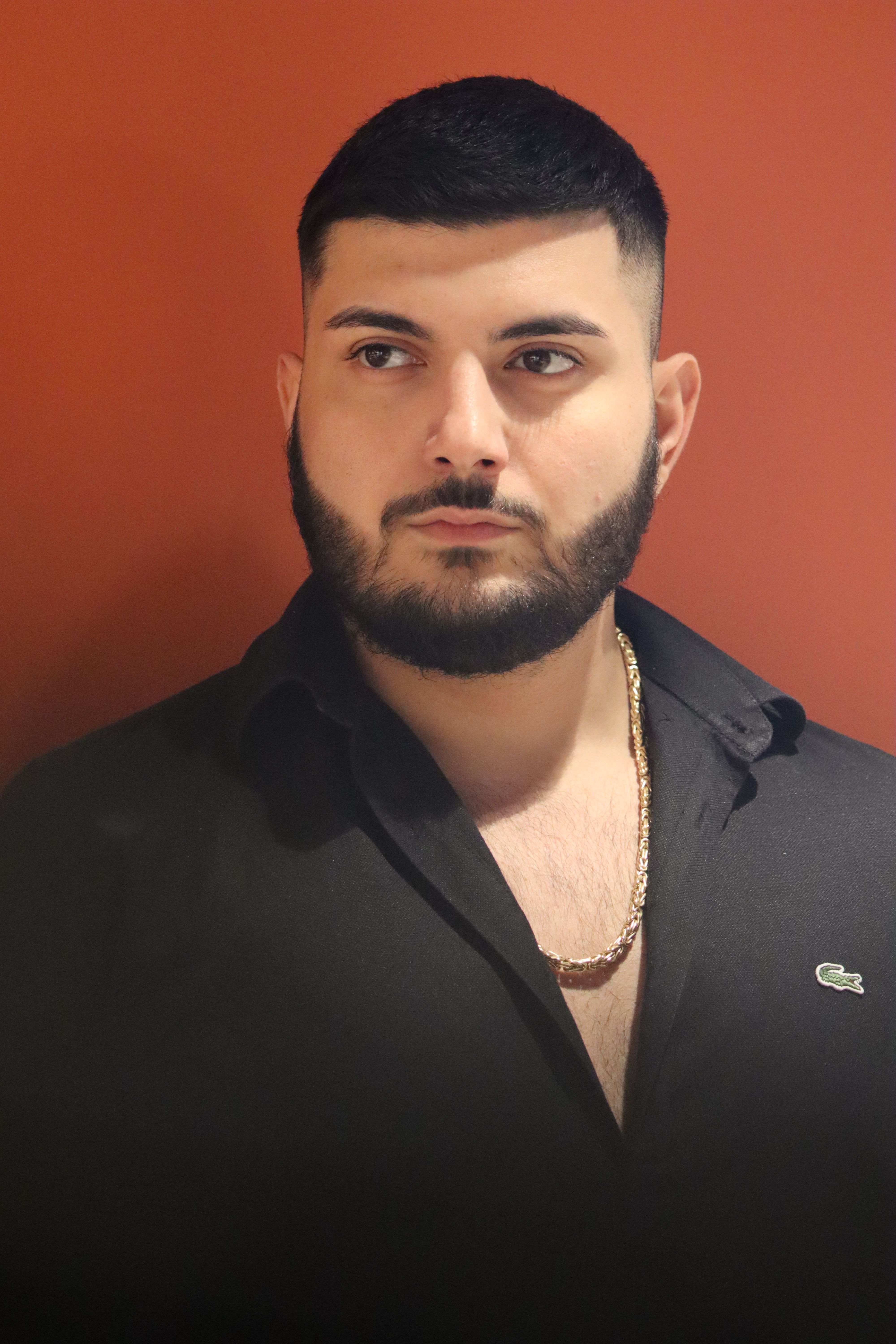 Portrait of a stylish young man with dark hair and a beard wearing elegant attire against a warm background.