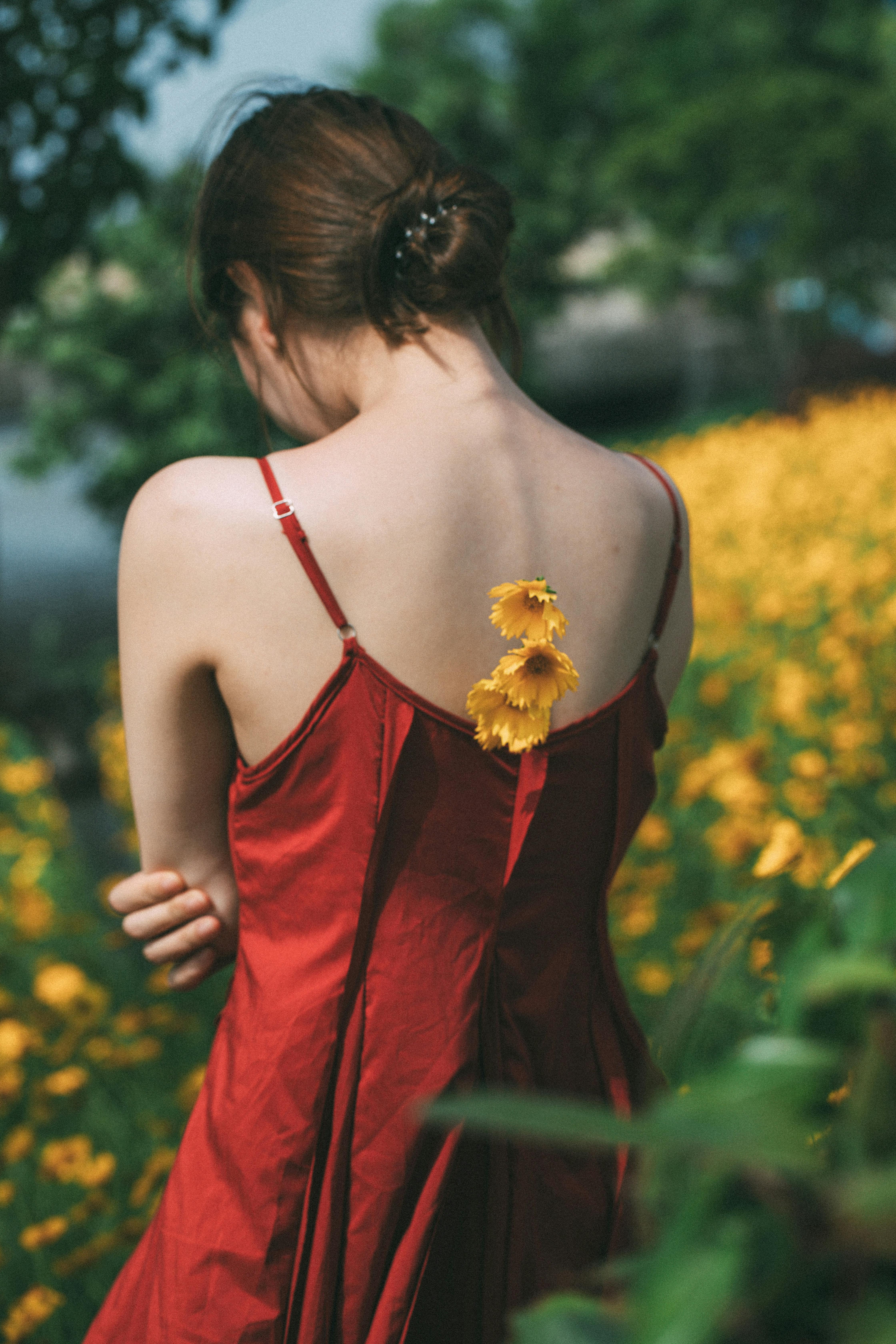 Back view of a woman in a red dress standing in a field of yellow flowers on a sunny day.