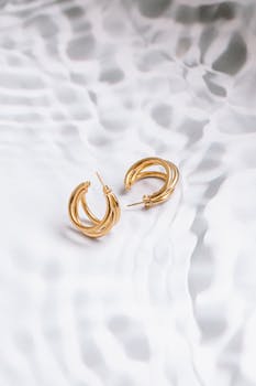 A pair of stylish gold hoop earrings captured on a wavy, textured background, highlighting their elegance.