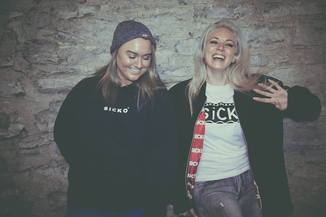 Two Woman Standing in Front of Wall While Smiling