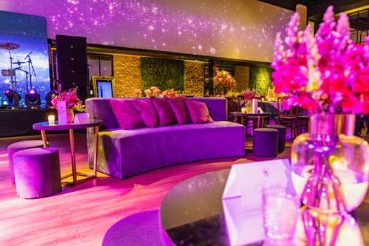 Chic event space featuring plush purple seating, ambient lighting, and floral arrangements.