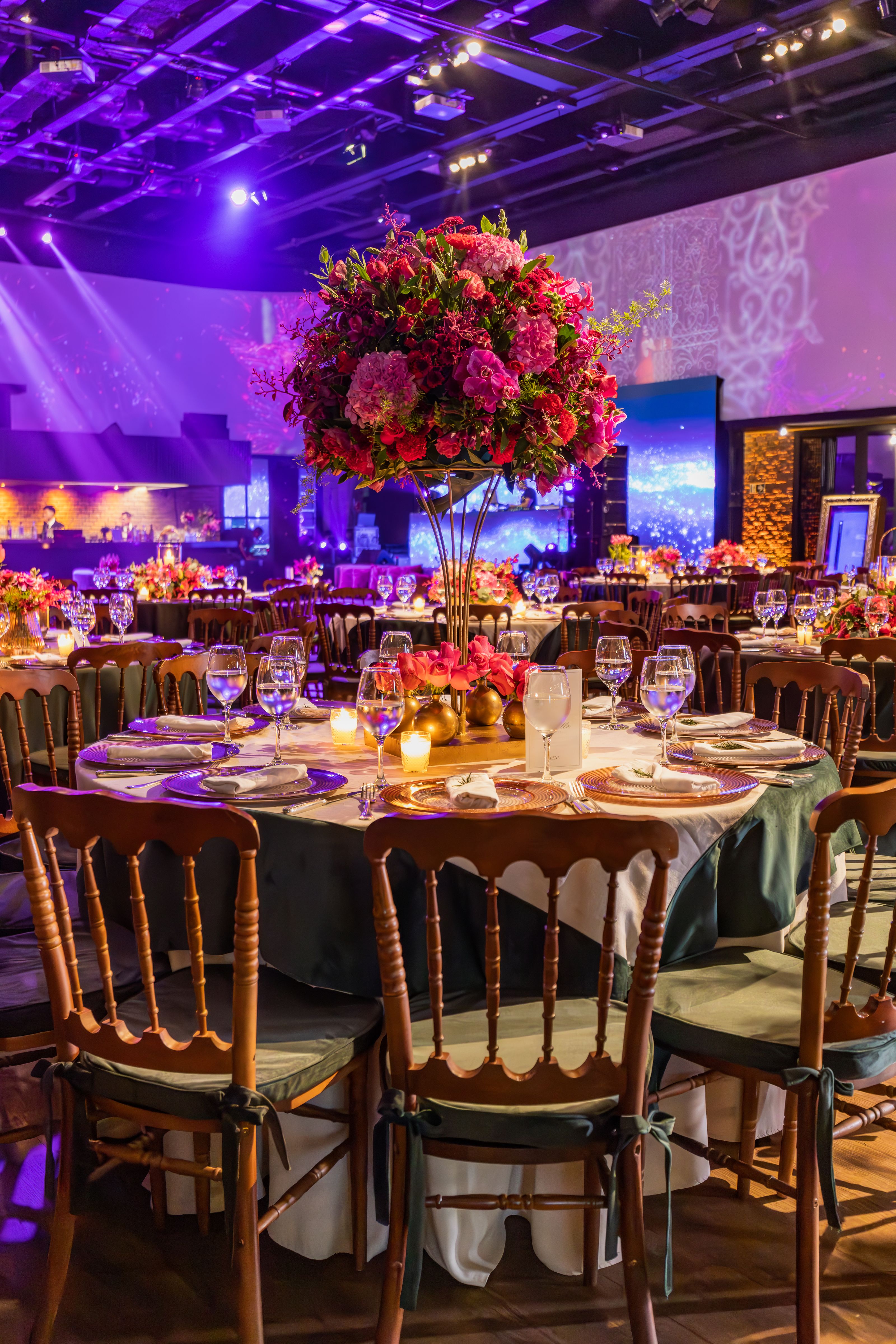 Recepção de casamento elegante com arranjos florais e elaboradas arrumações de mesa em um grande salão.