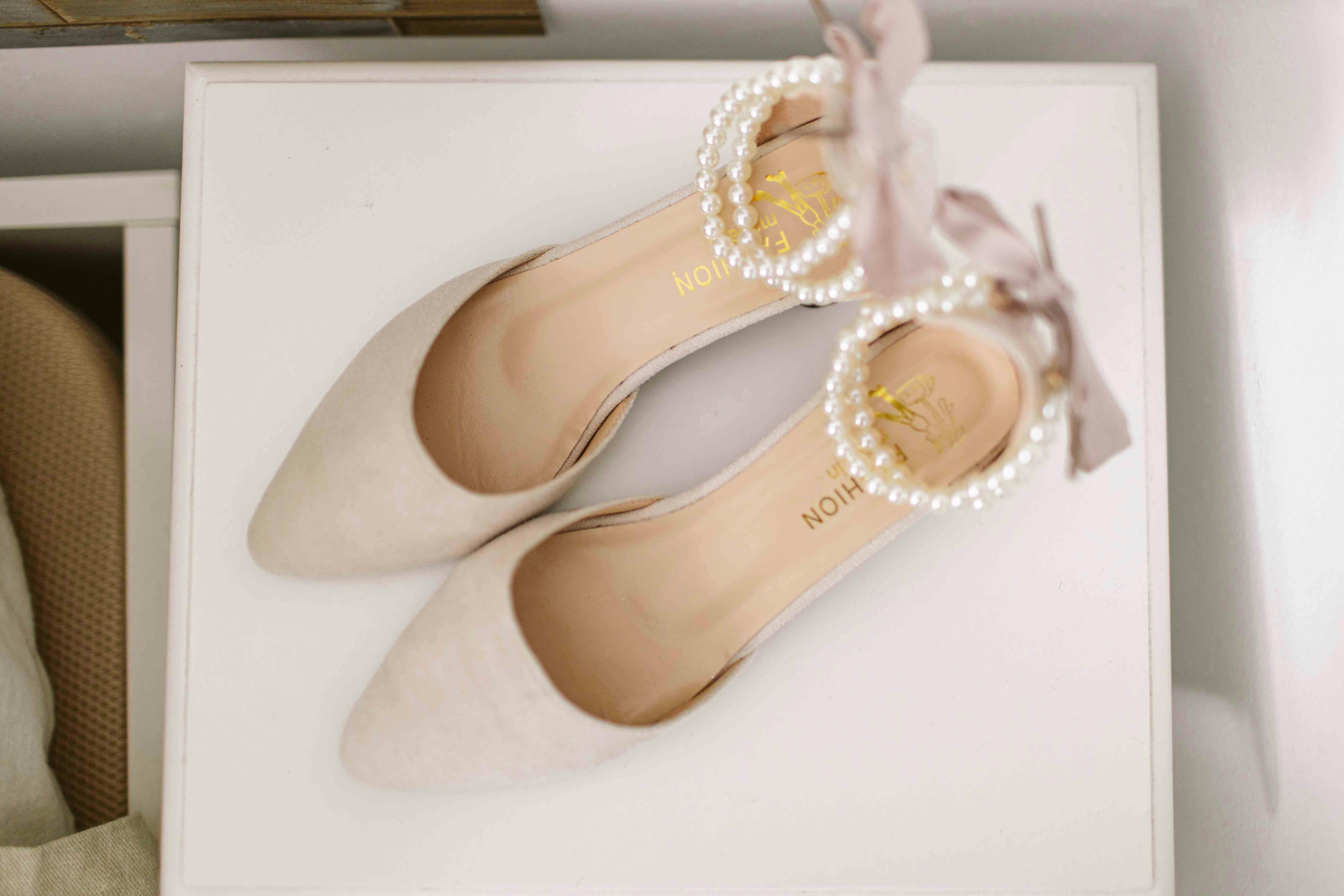 Top view of elegant bridal shoes with pearl and ribbon decor on a white surface, perfect for wedding fashion.