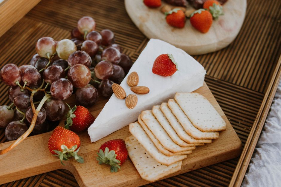 Elegant cheese platter with grapes, strawberries, and crackers on a wooden tray.