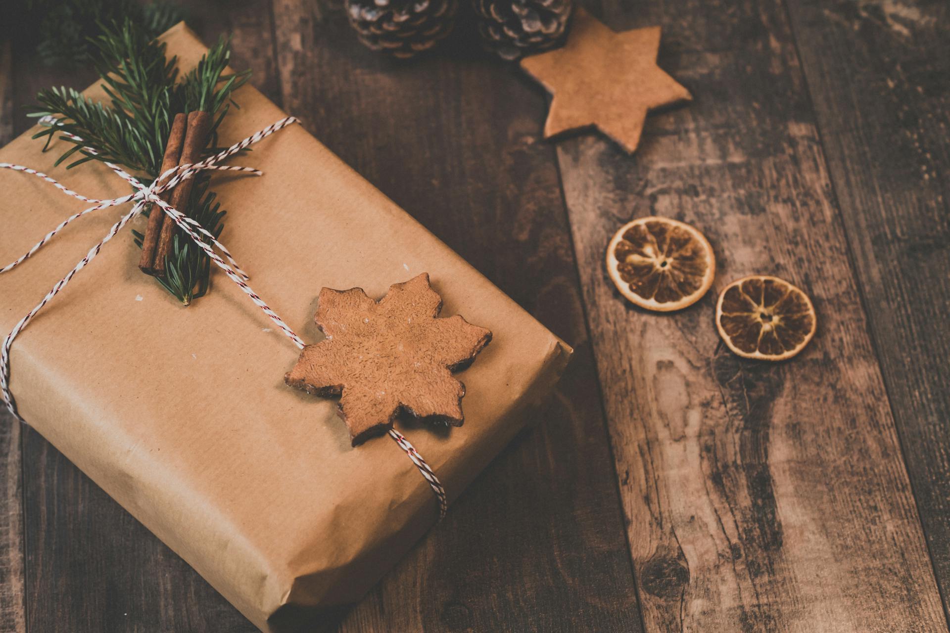 Wooden table with rustic Christmas gift wrapped in brown paper and adorned with natural elements.