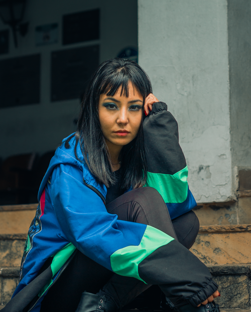Free Stylish woman with black hair sitting on steps in a colorful jacket. Stock Photo