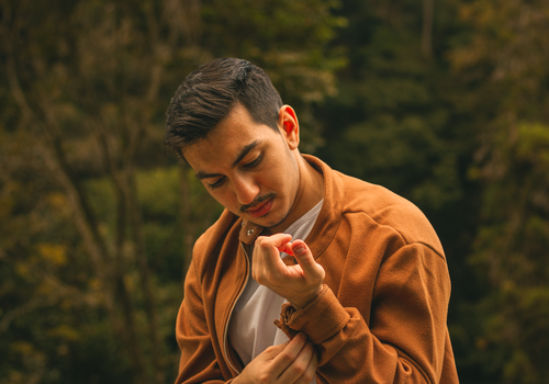 Free A man with short hair adjusting his jacket outdoors, showcasing a thoughtful pose against a natural background. Stock Photo