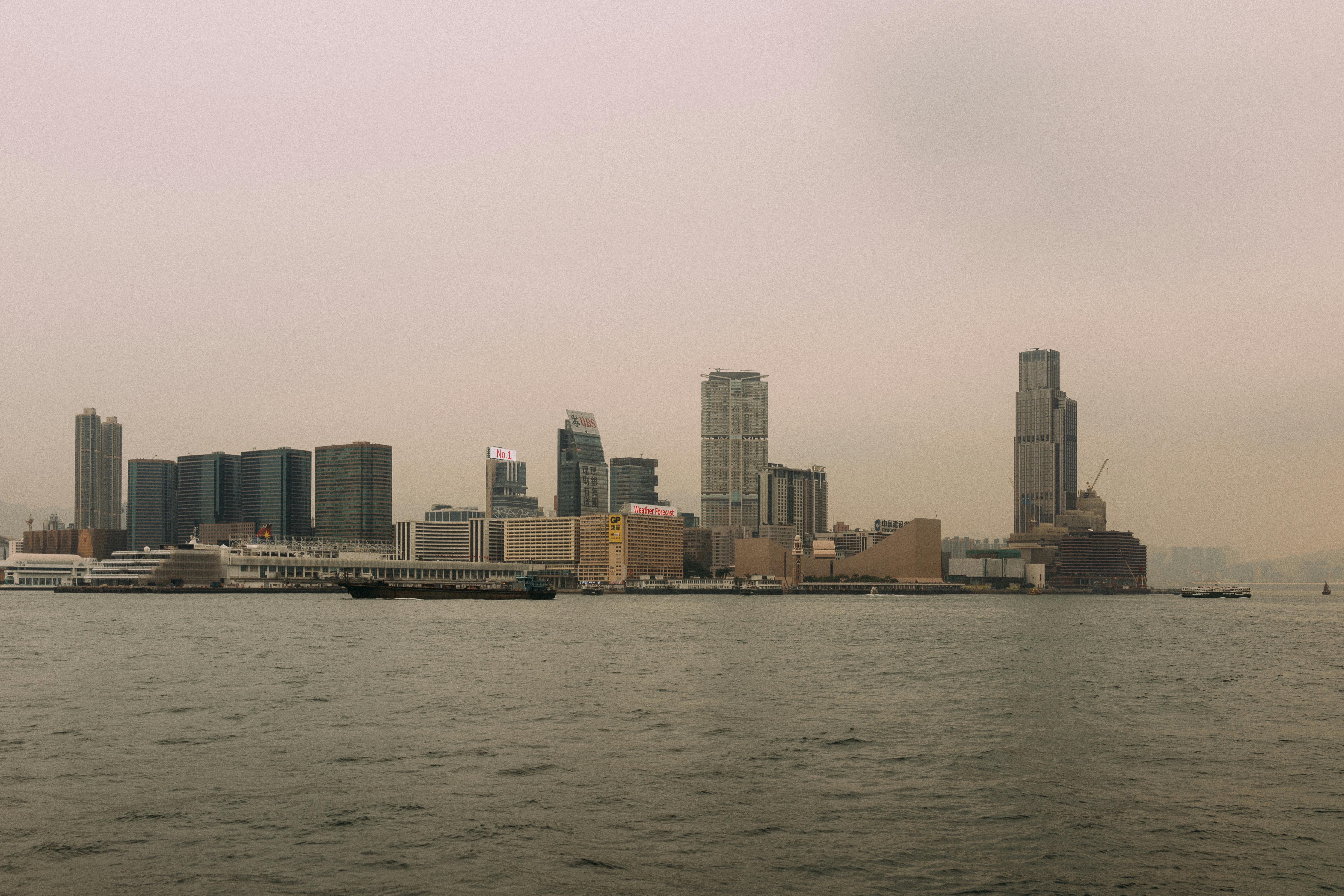 A city skyline with modern skyscrapers by the waterfront on a hazy day.