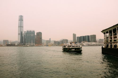 Free Ferry navigating the bustling waterfront of Hong Kong with modern skyscrapers in the background. Stock Photo