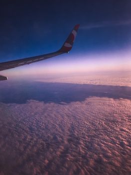 View from airplane window of colorful clouds and wing at sunset, showcasing travel and flight.