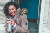 一位穿着冬衣、面带微笑的女人，拿着装有热饮的保温瓶，坐在蓝色的门旁