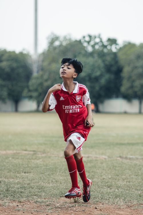 Free A young boy practicing soccer outdoors in a red sports jersey. Stock Photo