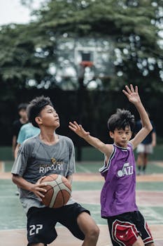 Two teenagers playing basketball on an outdoor court during the day. Action-packed and engaging.