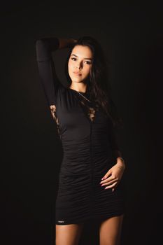 Striking studio shot of a woman posing elegantly in a black dress against a black background.