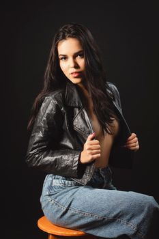 Captivating portrait of a woman posing in a leather jacket against a black background.