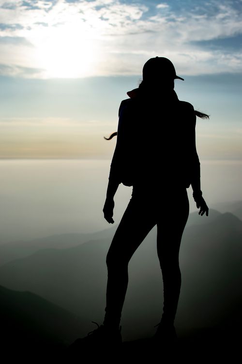 Free Silhouette of a woman on a mountain peak at sunset, capturing adventure and freedom. Stock Photo