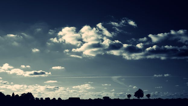Silhouetted landscape beneath an overcast sky, showcasing dramatic cloud patterns at dusk.