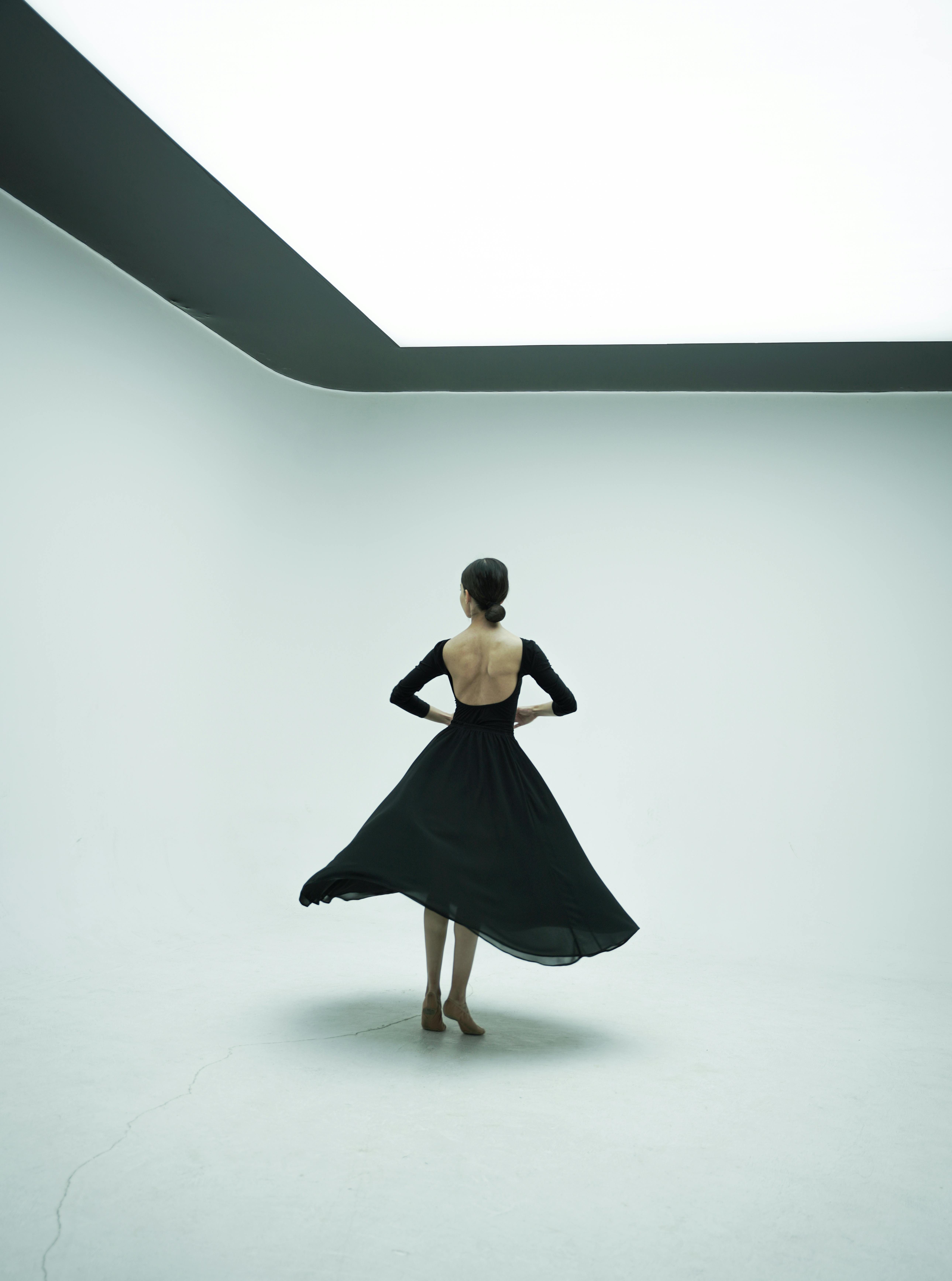 A ballerina gracefully poses in a minimalist white room, showcasing elegance and poise.