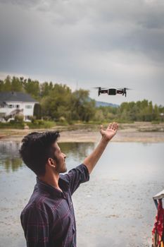 A young man pilots a drone near a serene water body in Srinagar, showcasing rural technology use.