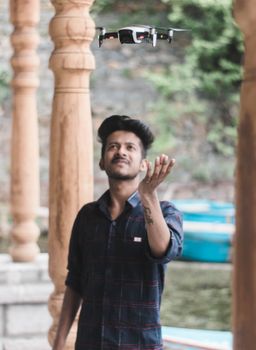 A young man skillfully operates a drone outdoors amidst ornate columns in Srinagar, showcasing modern technology in a traditional setting.