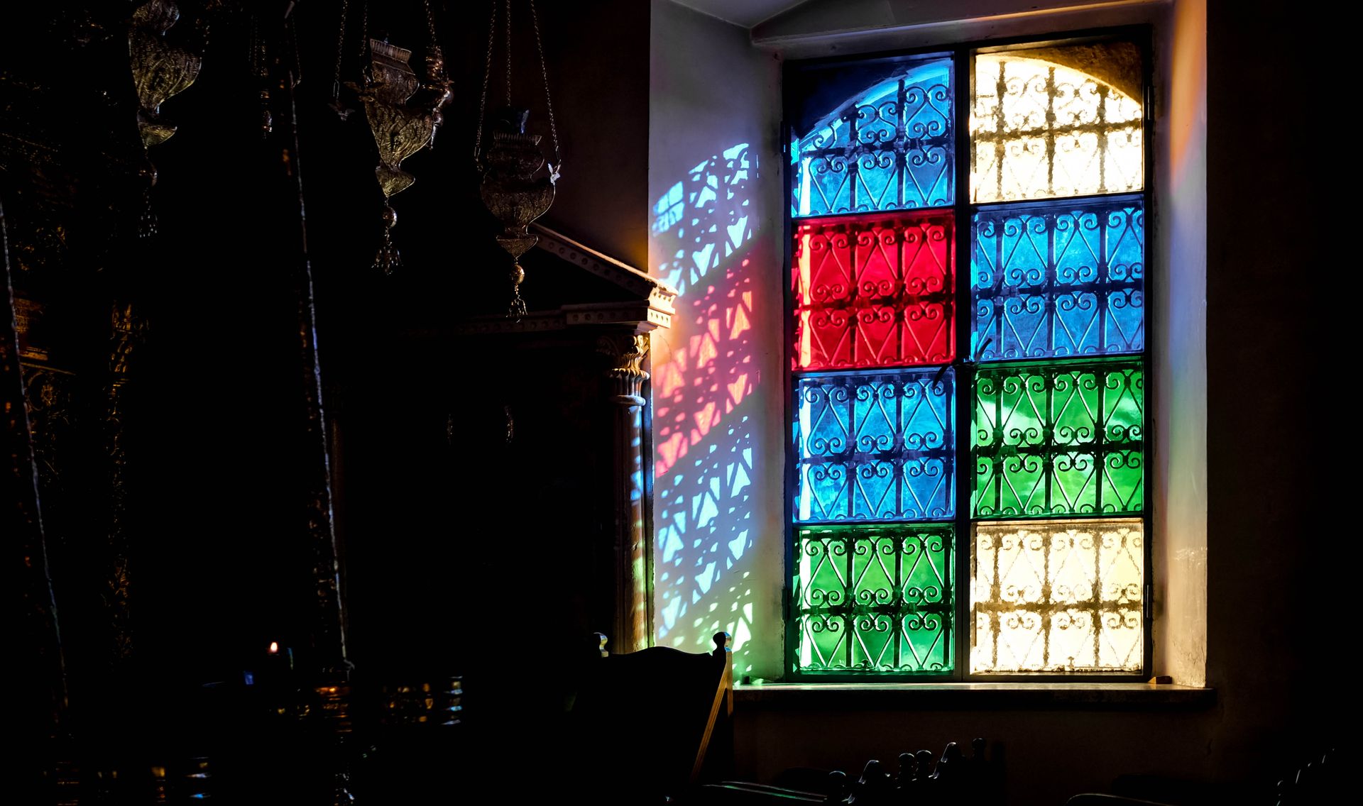 Colorful stained glass window casting vibrant shadows in a dimly lit room.