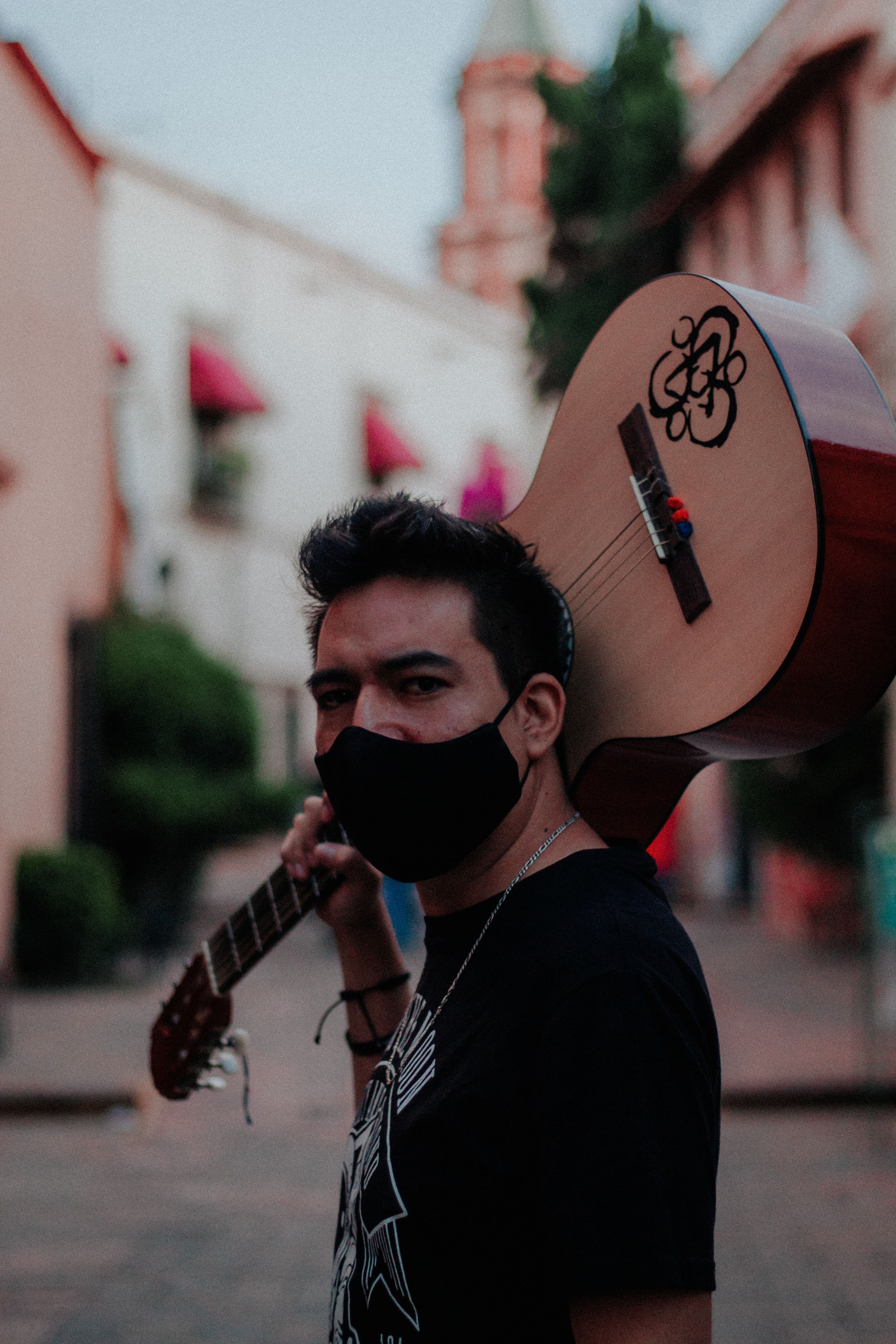 A man with a guitar and mask on a vibrant street in Santiago de Querétaro, Mexico.