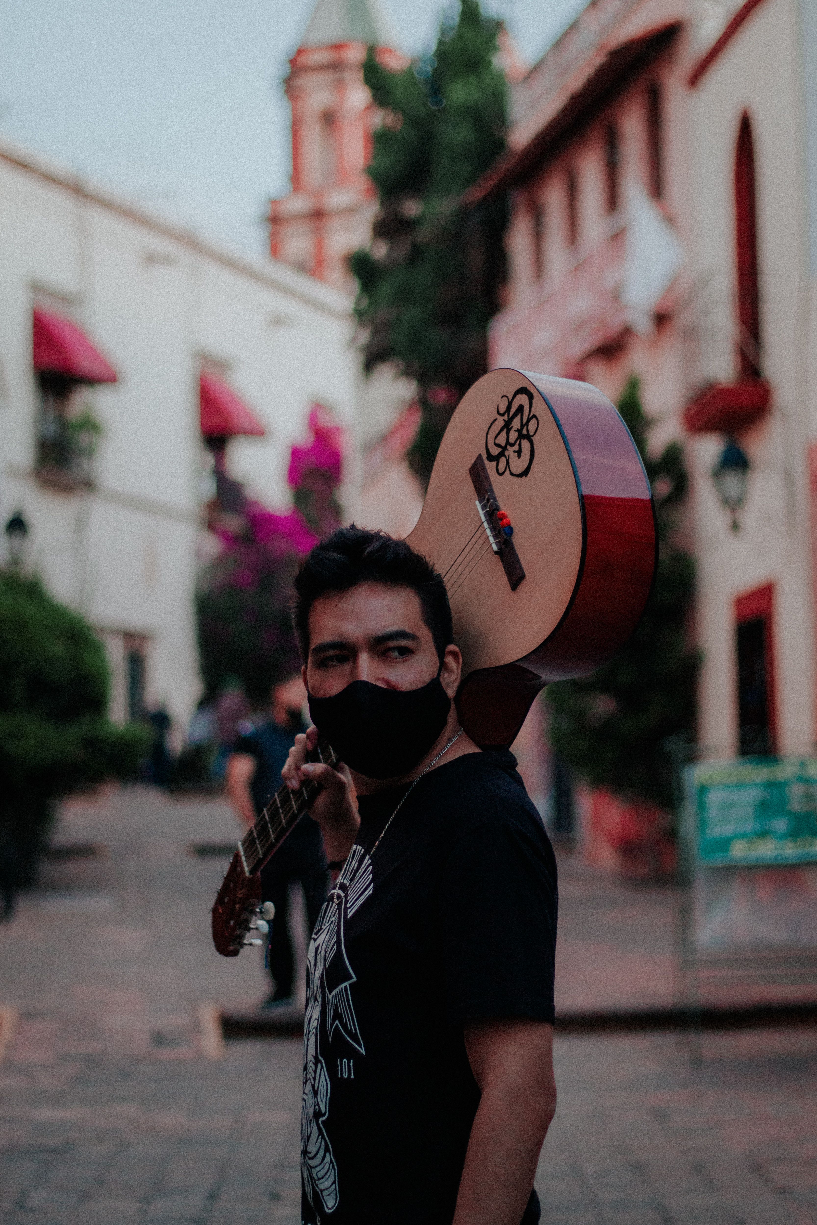 Man wearing a face mask carrying a guitar on a city street in Santiago de Querétaro, Mexico.