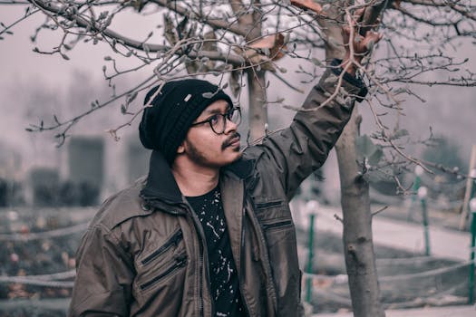 公园里，一个戴眼镜、穿冬装的人正在看树枝