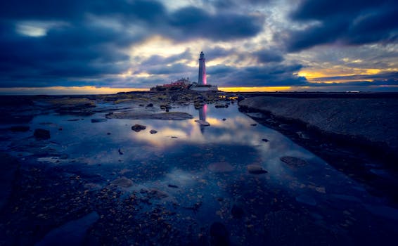 Dramatic sunset at St Mary's Lighthouse reflected in tidal pools, creating a stunning seascape.