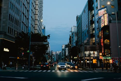Free Vibrant city street in the evening, highlighting urban life with buildings, cars, and bright neon signs. Stock Photo