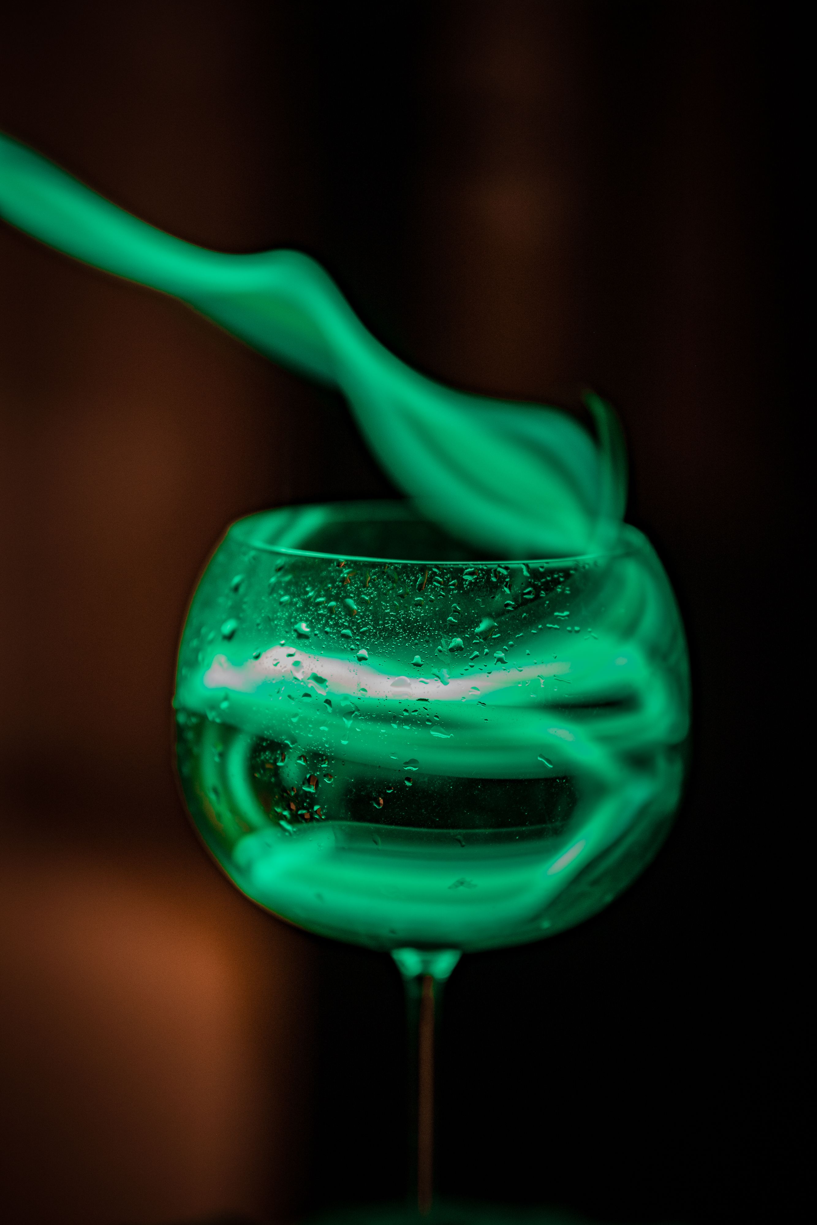 Artistic still life of swirling green smoke over a glass in a dark setting.