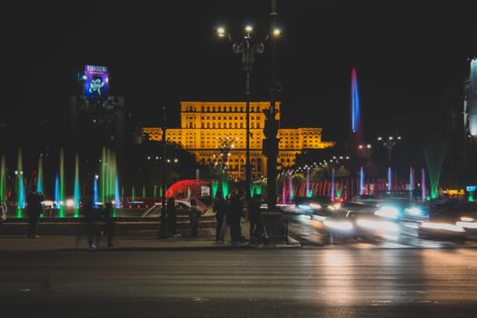 Nighttime view of Bucharest city with colorful fountains and blurred car lights.