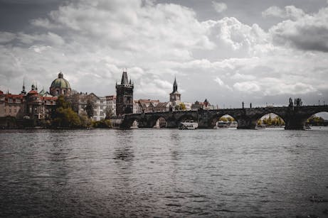 Iconic view of Charles Bridge spanning Vltava River with Prague's skyline, cloudy skies.